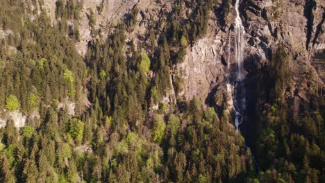 Aerial-drone-footage-pushing-in-from-a-distance-with-dreamy-views-of-Fallbach,-a-stunning-waterfall-in-Grindelwald,-Switzerland