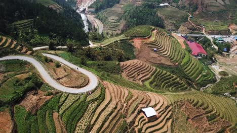 An-aerial-shot-looks-down-at-terraced-fields-and-shows-a-motorcycle-climbing-up-a-winding-road