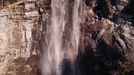 Aerial-drone-footage-raising-up-a-stunning-waterfall-with-beautiful-rainbow-reflections-at-Fallbach-in-Grindelwald-in-the-Swiss-Alps