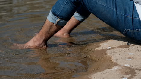 Close-up-static-shot-of-man-lying-by-river-with-bare-feet-in-water
