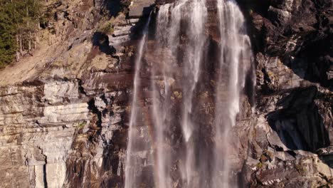 Aerial-drone-footage-raising-up-a-picturesque-waterfall-with-colorful-rainbow-reflections-at-Fallbach-in-Grindelwald-in-the-Swiss-Alps