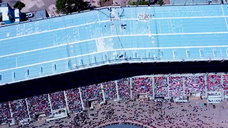 Birds-eye-above-view-top-aerial-over-revealing-the-stadium-grand-stand-where-rodeo-performers-present-themselves-while-crowds-cheer-them-as-they-approach-grandstand-audience-cheering-loud-and-proud