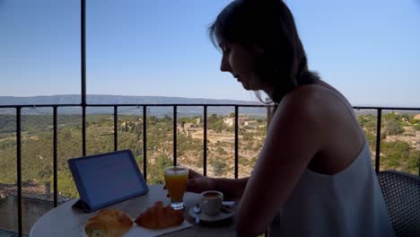 Mujer-Trabajando-Desde-Su-Ipad-En-El-Balcón-Del-Hotel-Mientras-Desayuna