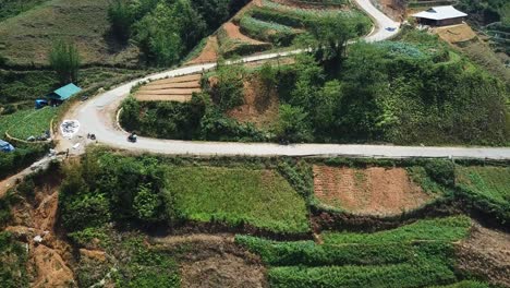 An-aerial-shot-follows-a-motorbike-up-a-winding-road-through-terraced-fields-towards-the-top-of-a-hill