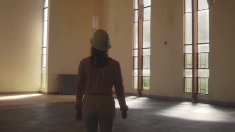 Female-architect-walking-with-a-white-hard-hat-entering-a-huge-room-during-an-observation