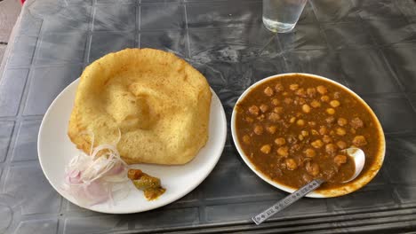 Top-shot-of-Indian-breakfast-cuisine-Chole-Bhature-or-Poori-with-chickpea-chana-masala-curry,-served-with-mixed-pickle-and-sliced-onion