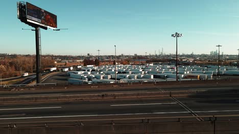 Trucks-driving-on-interstate-with-freight,-behind-the-road-is-a-truck-stop,-truck-drivers-parked-at-the-service-plaza-between-New-York-and-New-Jersey-on-I-95-aerial-footage-4k