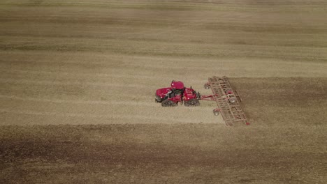 Luftaufnahme-Des-Großen-Traktors-Auf-Gleisen,-Der-Ein-Eggensystem-Zieht,-Um-Den-Boden-Des-Großen-Farmfeldes-Zu-Rekultivieren
