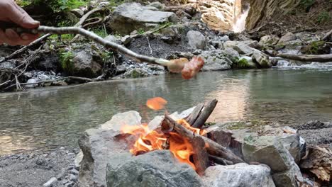 Guy-takes-well-done-sausages-from-camp-fire-to-eat-next-to-river