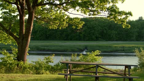 Low-drone-pushing-forward-over-a-picnic-table-and-turning-out-over-the-river-during-golden-hour-in-stratham,-nh-near-exeter