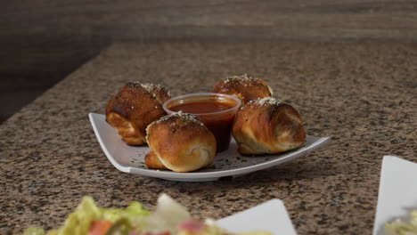 Four-garlic-knots-and-dipping-sauce-on-table-top,-slider-4K