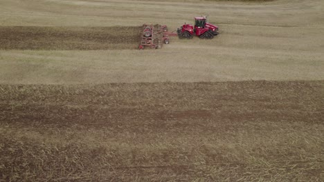 Aerial-trucking-shot-of-the-big-tractor-on-tracks-pulling-harrow-system-to-recultivate-soil-after-the-harvest