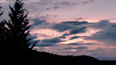 Aerial-on-zoom-lens-of-sunset-over-mountains-as-pine-trees-flys-past-in-the-foreground