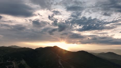 High-aerial-of-sun-setting-over-large-mountains-with-beautiful-cloud-formation