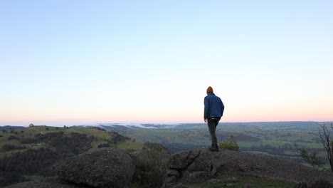 Ein-Mann-An-Einem-Aussichtspunkt-In-Der-Frühen-Morgensonne-Mit-Wolken,-Die-über-Die-Landschaft-Im-Hochland-Von-Victoria-Rollen