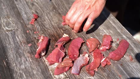 Male-hand-organizing-raw-boneless-deer-meat-filet-on-wooden-table---Sunny-outdoor-nature-clip-in-slow-motion