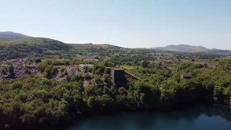 Dorothea-disused-overgrown-slate-mining-quarry-in-lush-dense-Snowdonia-mountain-woodland-aerial-rising-view