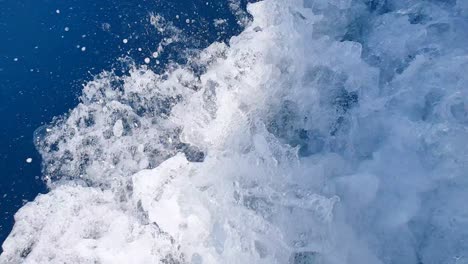 Fast-flowing-white-wash-spray-and-wake-in-deep-blue-ocean-water-from-a-motorboat-moving-at-pace,-close-up-of-whitewash-water