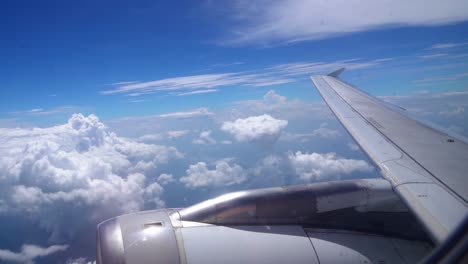 Shot-of-beautiful-fluffy-clouds-and-wing-of-airplane-visible-from-window-with-the-view-blue-sky-in-the-background