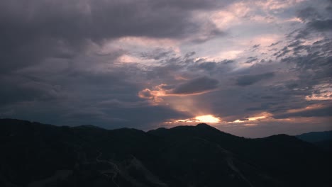 Aerial-hyperlapse-of-sun-setting-behind-clouds-and-mountains-as-dark-stormy-clouds-roll-in