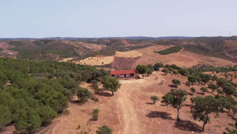 Antenne-Eines-Einsamen-Bauernhauses-Inmitten-Eines-Riesigen-Ackerlandes-In-Den-Abfallenden-Bergen-Von-Alentejo,-Portugal