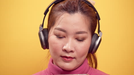 Wunderschöne-Asiatische-Junge-Frau-Der-Schönheit,-Die-Ein-Digitales-Tablet-Und-Eine-Streaming-anwendung-Für-Das-Fröhliche-Hören-Von-Musik-über-Kopfhörer-Mit-Entspanntem-Auf-Hellgelbem-Hintergrund-Verwendet