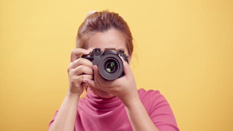 Brunette-young-Asian-woman-happy-and-joyous,-smiling-proudly-with-a-digital-camera-and-isolated-yellow-background