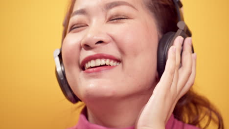 Brunette-young-Asian-woman-happy-listening-to-music-on-headphones-with-relaxed-on-bright-yellow-background