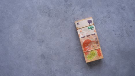 Mano-Colocando-Una-Pila-De-Billetes-Argentinos-De-$1000-Sobre-La-Mesa
