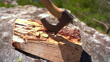 Blade-of-small-hiking-axe-inserted-in-firewood-log---Slowly-rotating-right---Sunny-day-slow-motion-handheld-nature-clip-with-shallow-depth-and-blurred-background
