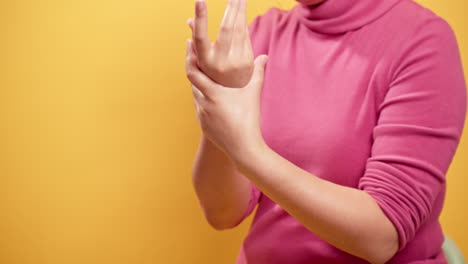 Close-up-women's-self-hands-applying-cream-on-hand-skin-and-rubbing-fingers-and-arm-with-a-yellow-background