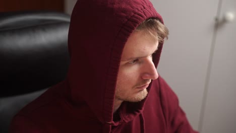 A-young-man-with-a-college-hoodie-on-sits-down-in-a-home-office-chair-and-proceeds-to-execute-some-code-on-a-computer