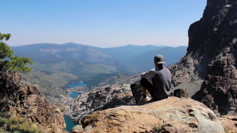 Young-man-sits-on-top-of-mountain-and-looks-down-on-scenic-lake-in-the-Sierra-Nevada-Mountain-Range-near-Lake-Tahoe-California