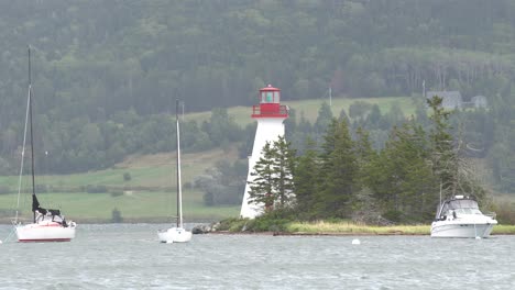 It-is-a-beautiful-lighthouse-with-3-sailboats-in-the-water-with-a-lot-of-trees-behind-it