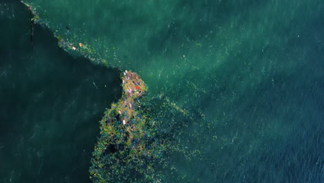 Blue-ocean-water-covered-in-rubbish-island,-aerial-top-down-view