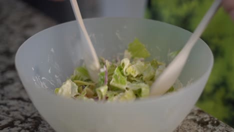 Mixing-healthy-salad-in-large-bowl-with-greens-using-two-salad-spoons,-close-up