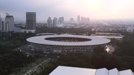 Wide-panoramic-of-GBK-Stadium-skyline-buildings-at-dusk-in-Jakarta,-aerial