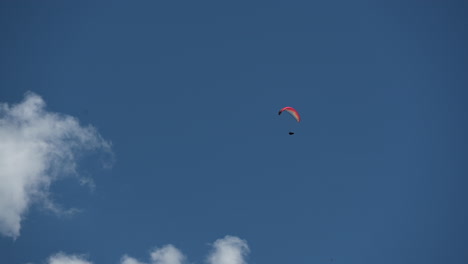 Ein-Bunter-Fallschirm-Fliegt-Am-Mittag-In-Einem-Blauen-Himmel-Mit-Ein-Paar-Wolken-über-Den-Schweizer-Alpen