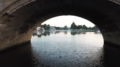 Impressive-drone-shot-of-Henley-on-Thames,-flying-through-the-bridge-at-sunrise