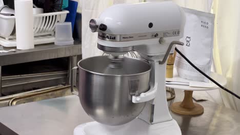 Pastry-chef-set-the-electric-mixer-mixing-egg-white-and-sugar-until-it-is-glossy-peak-and-stiff-peak,-preparing-meringue-buttercream,-commercial-kitchen-setting-close-up-shot