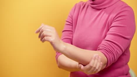 Close-up-women's-hands-applying-cream-on-hand-skin-and-rubbing-fingers-and-arm-with-a-yellow-background