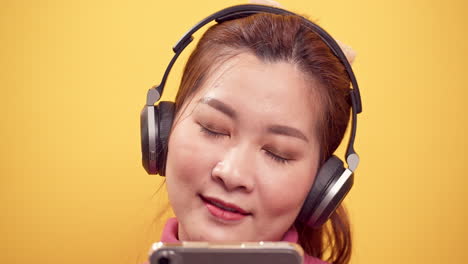 Primer-Plano-De-Una-Hermosa-Joven-Asiática-Usando-Una-Tableta-Digital-Y-Una-Aplicación-De-Transmisión-Para-Escuchar-Música-Feliz-En-Los-Auriculares-Con-Un-Fondo-Amarillo-Brillante-Y-Relajado