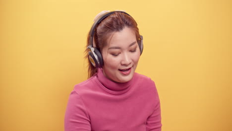 Asiatische-Frau,-Die-Ein-Digitales-Tablet-Und-Eine-Streaming-anwendung-Verwendet,-Um-Musik-über-Kopfhörer-Zu-Hören,-Während-Sie-Den-Hund-Entspannt-Auf-Hellgelbem-Hintergrund-Spielt