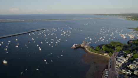 Aerial-view-ovelooking-sunlit-boats-and-the-Mayflower-II-ship,-summer-evening-on-the-coast-of-Plymouth,-USA