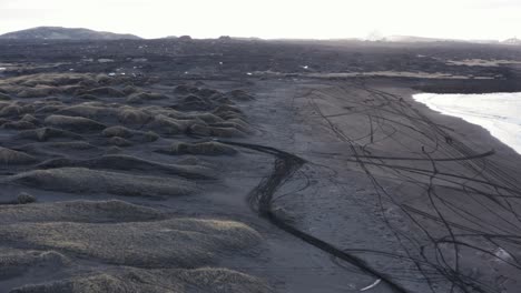 Sandvik-black-volcanic-beach-with-motorcross-tire-tracks-during-sunrise,-aerial