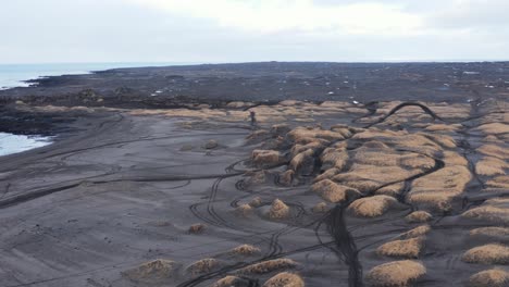 Grassy-dunes-at-black-volcanic-sand-beach-Sandvik-with-motorcross-tire-tracks