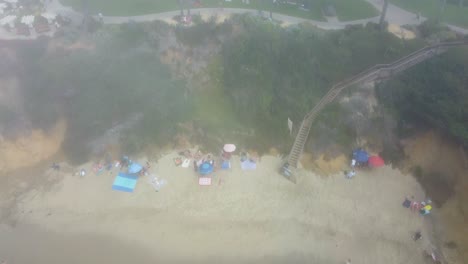 Aerial-View-of-Morning-Fog-Above-Laguna-Beach-and-Beachfront-Park-With-Group-of-People-Having-Morning-Workout,-California-USA,-Revealing-Tilt-Up-Drone-Shot