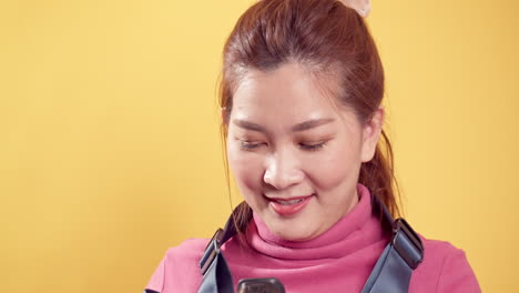 Fröhliche,-überschwängliche-Asiatische-Frau-In-Rosafarbener-Kleidung-Mit-Einer-Digitalkamera-Vor-Einem-Isolierten-Gelben-Hintergrund