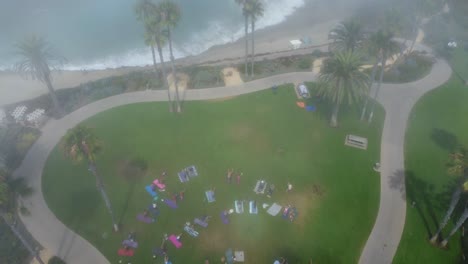 Top-Down-Aerial-View-of-Morning-Fog-and-Group-of-People-Having-Morning-Workout-and-Stretching-in-Park-by-Pacific-Ocean,-Laguna-Beach-CA-USA,-High-Angle-Drone-Shot