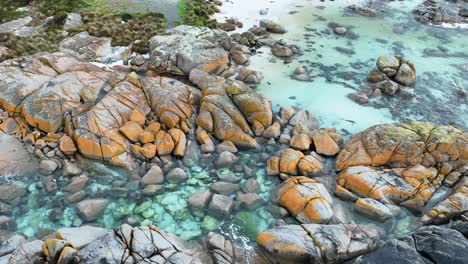 Bright-orange-boulders-along-a-coastline-stand-out-against-the-clear-blue-water